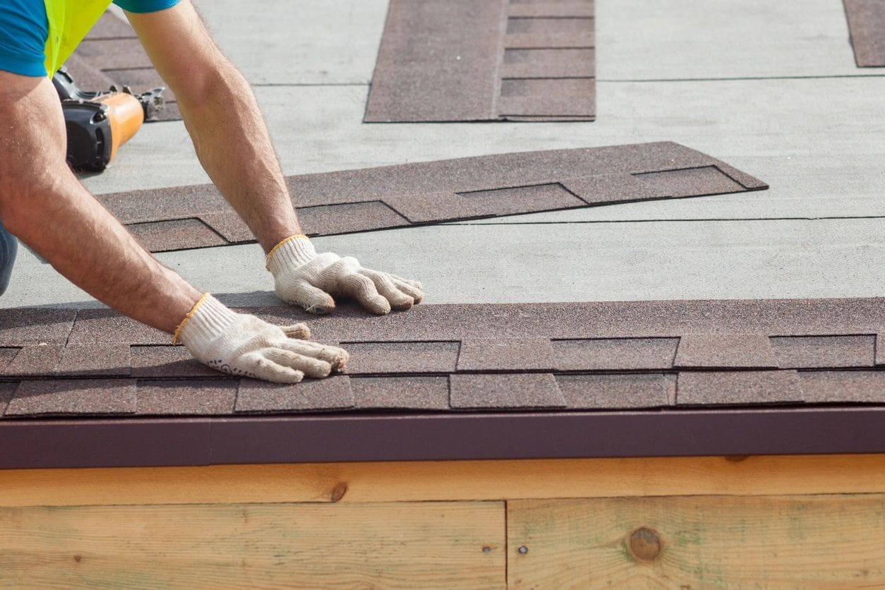 Worker installing asphalt shingles on roof.